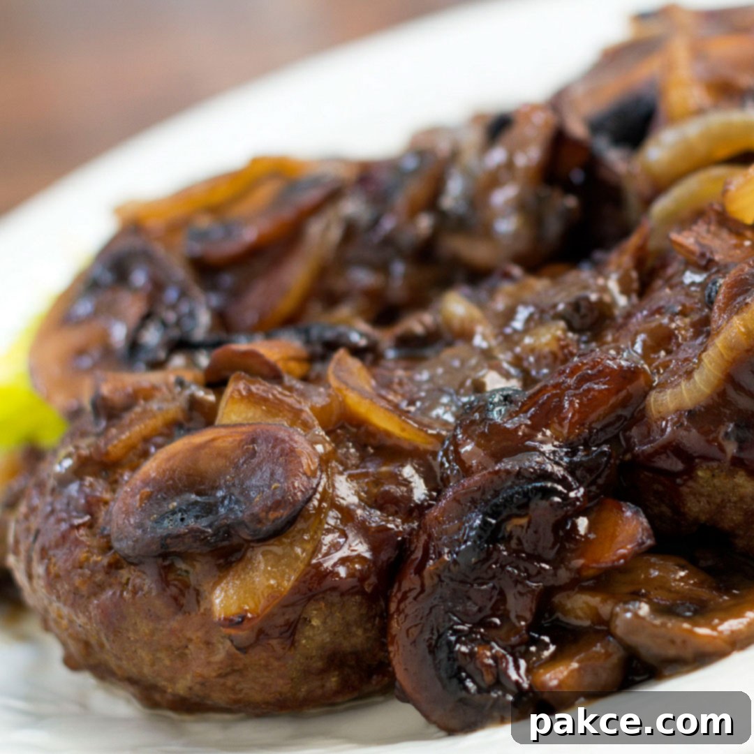 Juicy hamburger patty covered with sliced mushrooms, onions, and a rich brown gravy, served as a classic comfort food.
