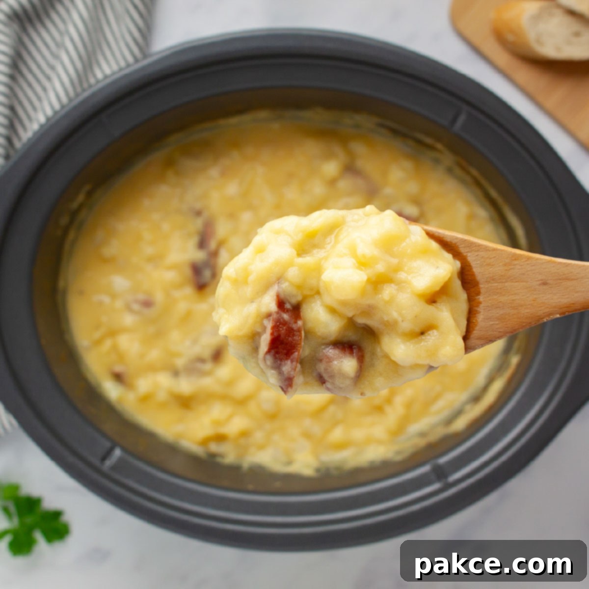Slow Cooker Cheesy Kielbasa and Potato Soup 5 Close-up of a spoonful of potato soup with kielbasa pieces on a wooden spoon held over a crockpot of the soup.