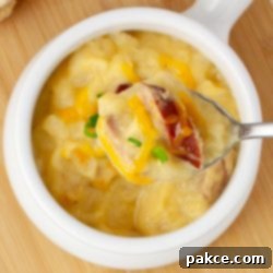 Slow Cooker Cheesy Kielbasa and Potato Soup 7 Closeup of a spoonful of potato soup with kielbasa garnished with shredded cheddar cheese and sliced green onion held above a crock of the soup.