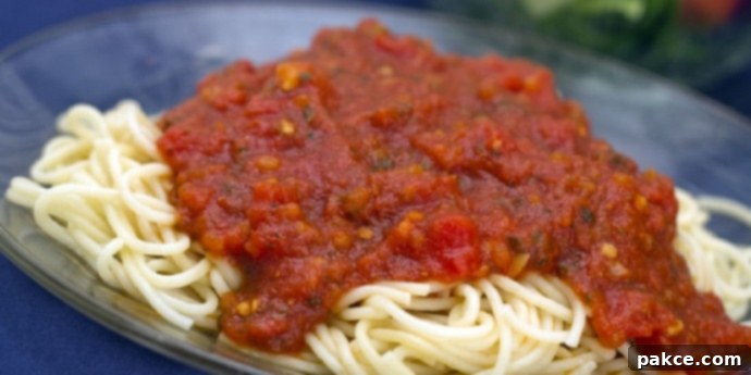 A vibrant red homemade marinara sauce generously covering a pile of cooked spaghetti noodles on a blue plate, ready to be enjoyed. Fresh green herbs garnish the dish.