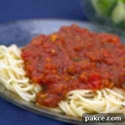 Easy Slow Cooker Marinara 2 A closer look at a plate of cooked spaghetti noodles generously coated with vibrant red crockpot marinara sauce, garnished with fresh herbs and a sprinkle of cheese.