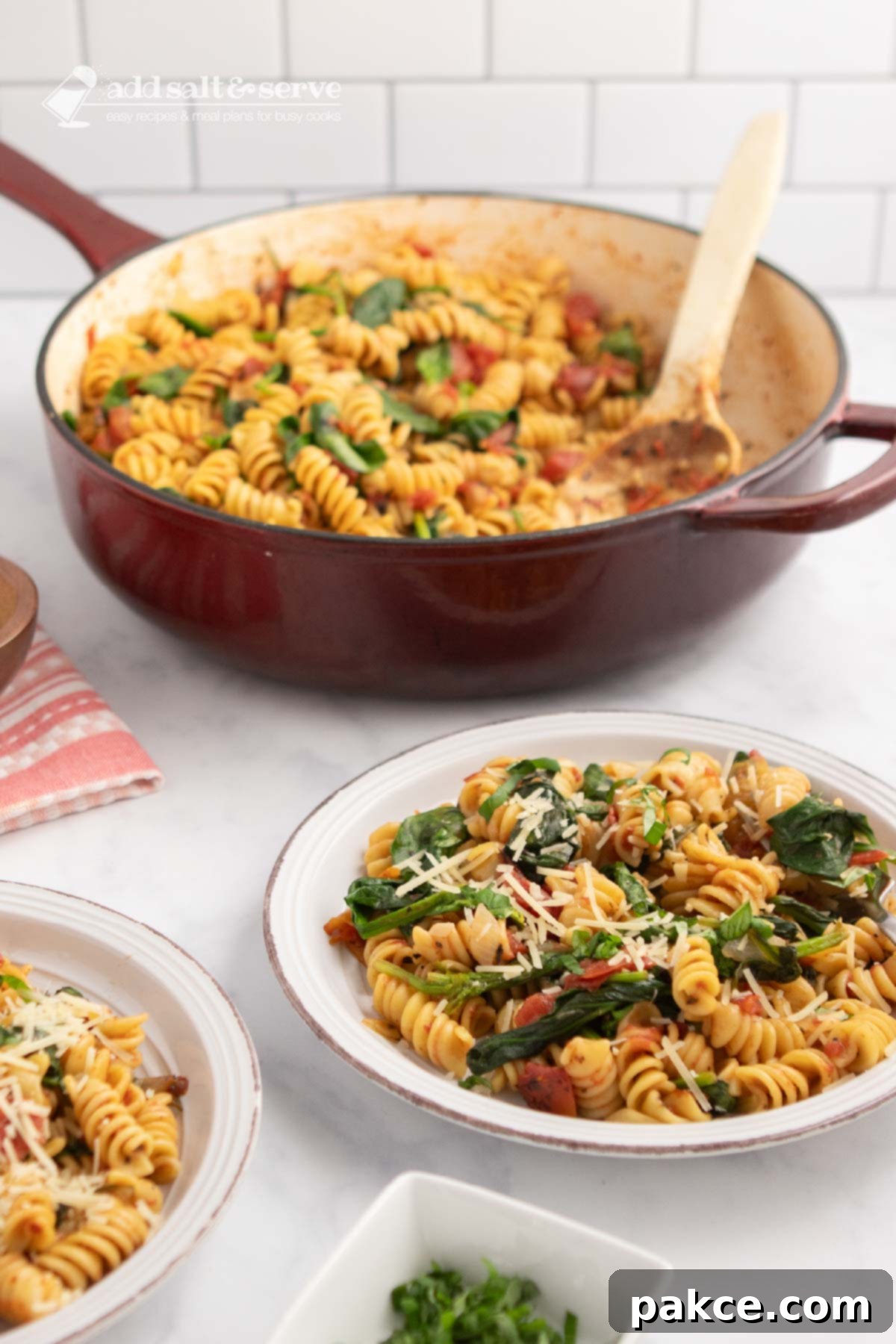 One-Pan Tomato Spinach Pasta 6 Plate of tomato Spinach Pasta garnished with Parmesan cheese and fresh basil strips on a counter beside the pan of the full dish.