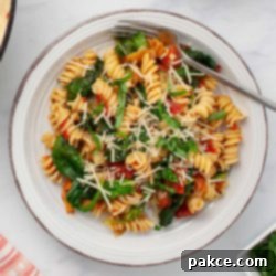 One-Pan Tomato Spinach Pasta 8 Plate of tomato Spinach Pasta garnished with Parmesan cheese and fresh basil strips.