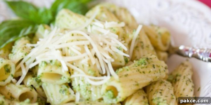 Pasta with Homemade Pesto Rigatoni on a white plate topped with shredded parmesan cheese and pesto.
