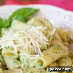 Rigatoni on a white plate topped with shredded parmesan cheese and pesto.