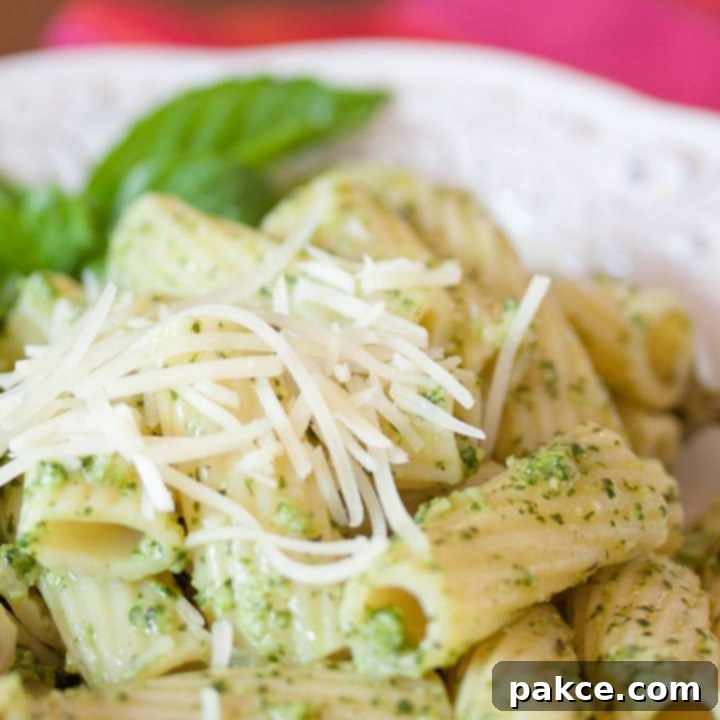 Rigatoni on a white plate topped with shredded parmesan cheese and pesto.