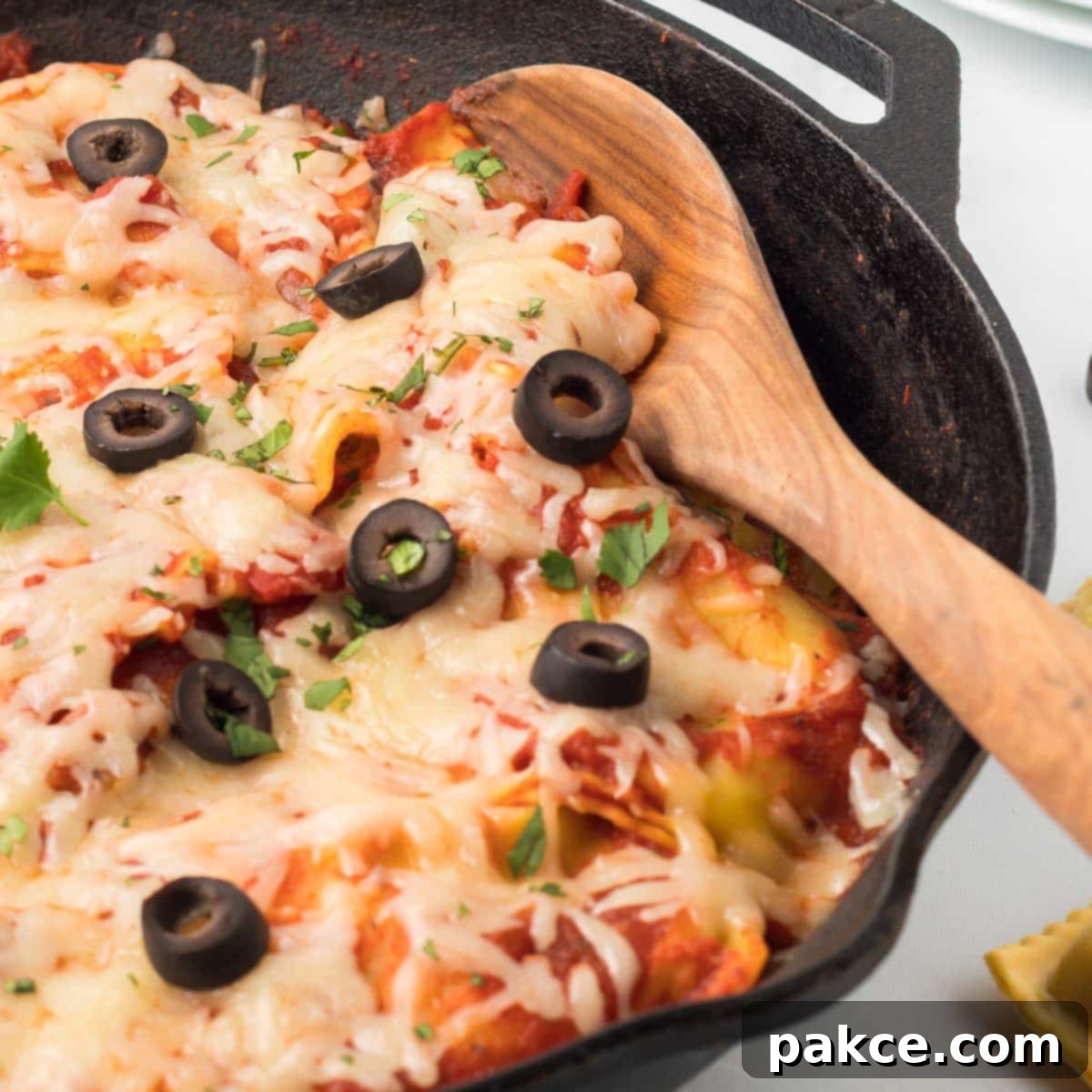 Fiesta Ravioli 2 Cast iron skillet with cooked ravioli mixed with salsa, herbs, and tomato sauce and topped with cheese, black olives, and cilantro, ready to serve.