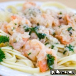 Garlic Butter Shrimp Scampi 2 White plate with shrimp, minced garlic, and parsley on a bed of fettuccine