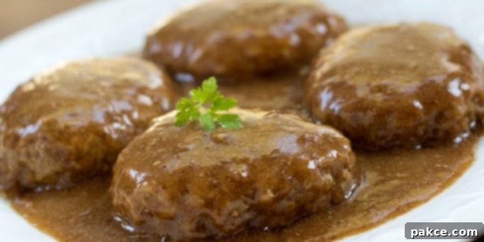 Simple Salisbury Steak White plate with hamburger patties covered with rich brown gravy and garnished with a sprig of fresh parsley.