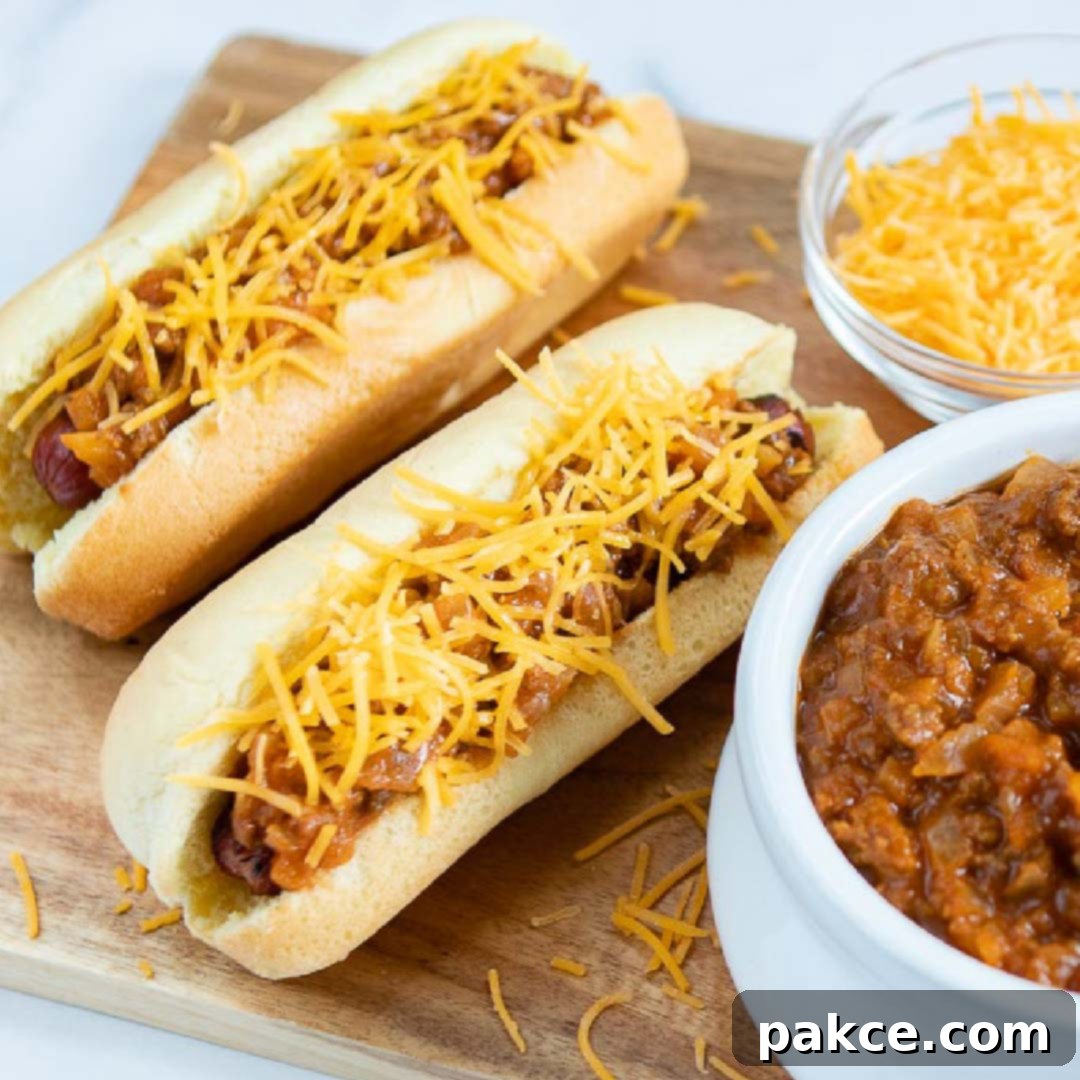 Two hot dogs in buns topped with chili and shredded cheese, a bowl of shredded cheese, and a bowl of chili.