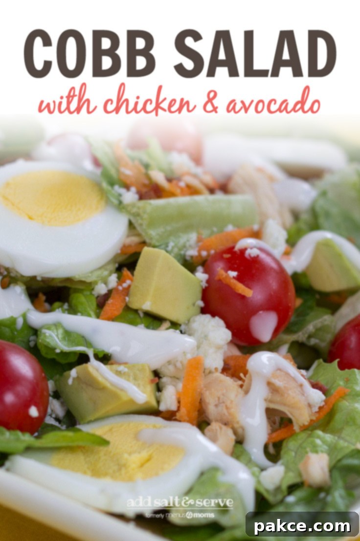 Cobb Salad artfully arranged in a large serving bowl, showing layers of fresh greens, diced chicken, sliced hard-boiled eggs, grape tomatoes, avocado, crumbled blue cheese, and turkey bacon.