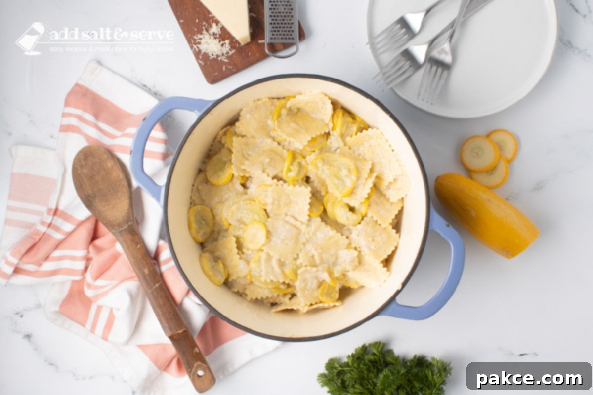 20-Minute Velvety Summer Squash Ravioli 9 Dutch oven with cooked cheese ravioli mixed with Parmesan cheese and sautéed summer squash and onion beside a wooden spoon and surrounded by fresh squash, a bunch of parsley, and a block of fresh Parmesan cheese.