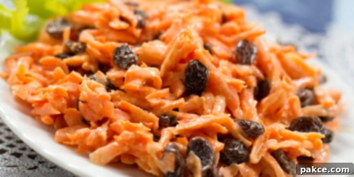 Carrot Raisin salad on a white plate garnished with celery leaves