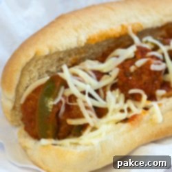 Classic Homemade Italian Meatball Subs 2 Meatballs, sauce, shredded mozarrella cheese, and strips of bell peppers on a hot dog bun, all on a white plate.
