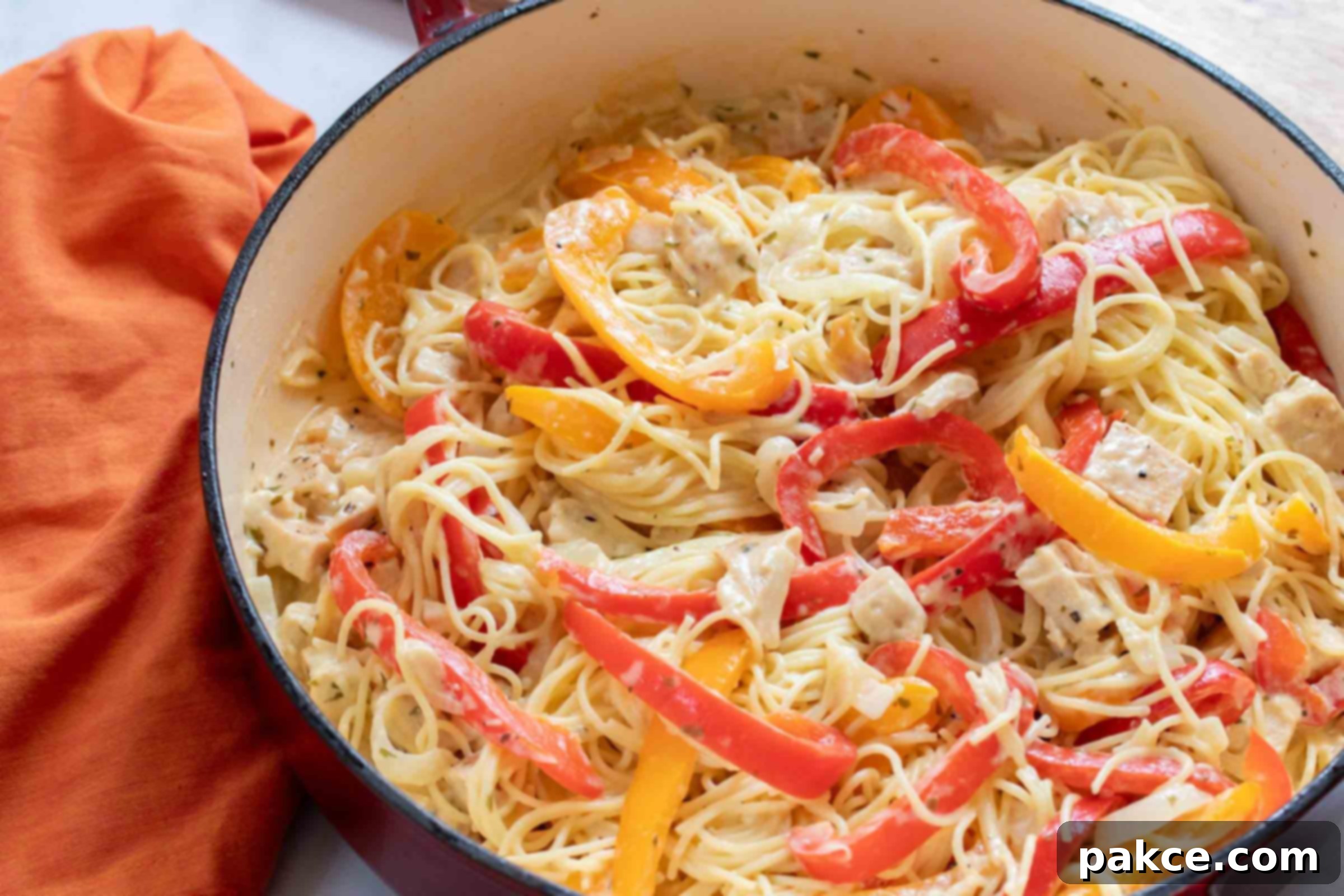 Chicken Pepper Pasta A large skillet filled with creamy pasta, diced chicken, sliced onion, and strips of red and yellow bell peppers, perfectly cooked and ready to be served.