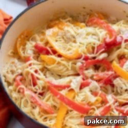 Chicken and Bell Pepper Pasta 3 Pasta with chicken, sliced onion, and strips of red and yellow bell peppers cooked in a white sauce in a skillet, representing the finished Creamy Chicken Pepper Pasta dish.