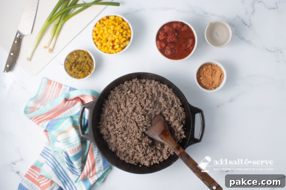 Zesty Mexican Pasta 4 A cast iron skillet with cooked ground beef and a wooden spoon, surrounded by small bowls of green chiles, Mexi-corn, fire-roasted diced tomatoes, taco seasoning, and water – all the ingredients for the sauce.