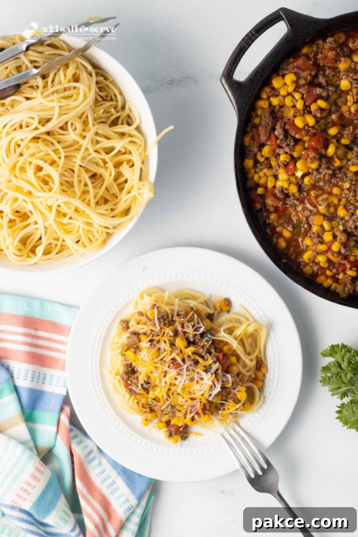 Zesty Mexican Pasta 9 A plated serving of Mexican Spaghetti garnished with shredded cheese and fresh herbs, beside a bowl of cooked spaghetti and a pot of the rich Mexican Spaghetti sauce, all on a kitchen counter.