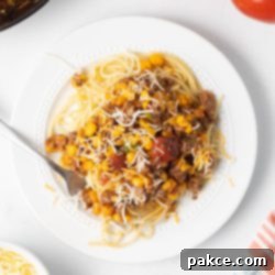 Zesty Mexican Pasta 10 A beautifully presented plate of Mexican Spaghetti topped with shredded Mexican blend cheese and a sprig of cilantro, capturing its delicious appeal.