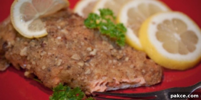 Pecan crusted salmon on a red plate with a fork, garnished with lemon slices and sprigs of parsley.