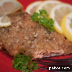 Nutty Pecan Salmon Delight 2 Pecan crusted salmon on a red plate with a fork, garnished with lemon slices and sprigs of parsley.