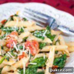 Vibrant Carbonara with Spinach and Tomatoes 2 White plate with penne pasta, cooked baby spinach, cherry tomatoes, and shredded mozzarella cheese. There is a fork on the plate.