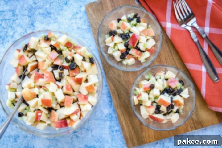Overhead view of salad with chopped apples, raisins, and celery with a coral plaid towel and two forks.