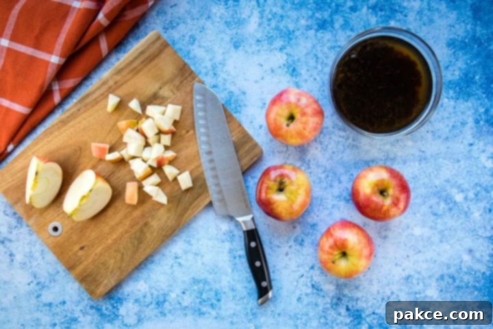 apple-raisin-salad-ip-6-min Overhead view of a chopping board with chopped apple and a knife, four apples to the side, a bowl of raisins soaking in water, all on a blue surface with a coral towel laying to the side.