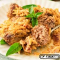 A plate of meatballs in a creamy red sauce with orzo with a meatball cut open on a fork.